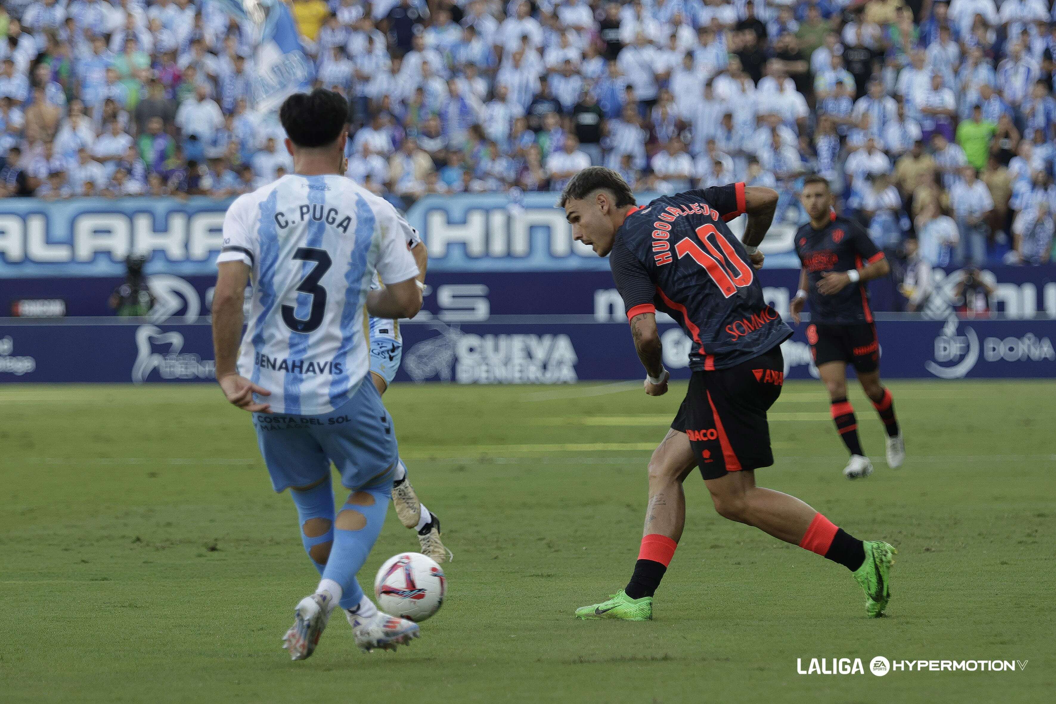 Carlos Puga, de espaldas, defiende a Hugo Vallejo en el Málaga - Huesca (Foto: LALIGA).