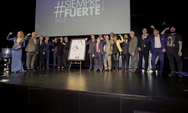 Premiados y autoridades posan junto al cuadro de Antonio Montiel haciendo el gesto de Pablo Ráez.