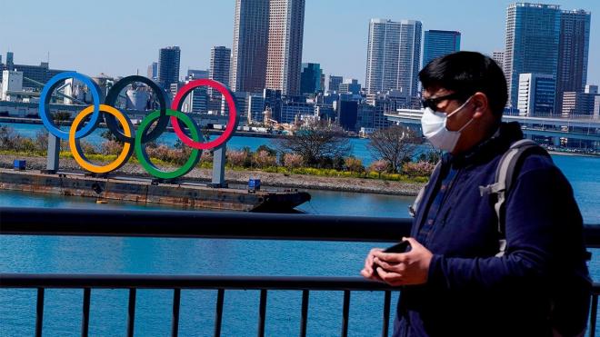 Una persona con mascarilla pasa por delante del logo de los Juegos Olímpicos de Tokio 2020.
