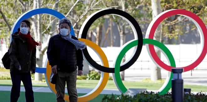 Dos individuos, con mascarillas ante el icono de los Juegos Olímpicos.