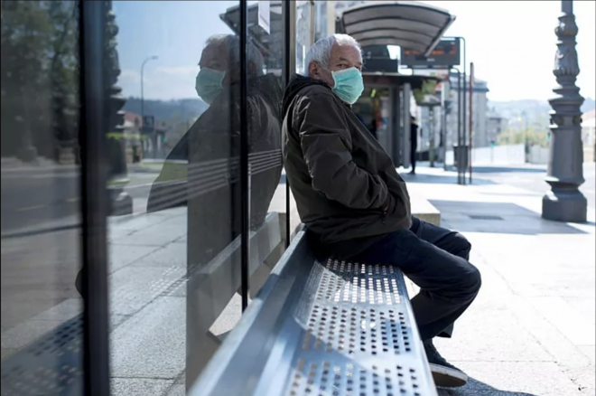 Un hombre con mascarilla por el coronavirus espera en una parada de autobús en Orense (Foto: EFE).