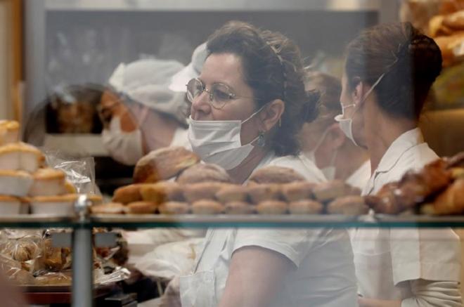 Trabajadoras protegidas con mascarillas atienden a los clientes en una panadería de Valencia (Foto: EFE).