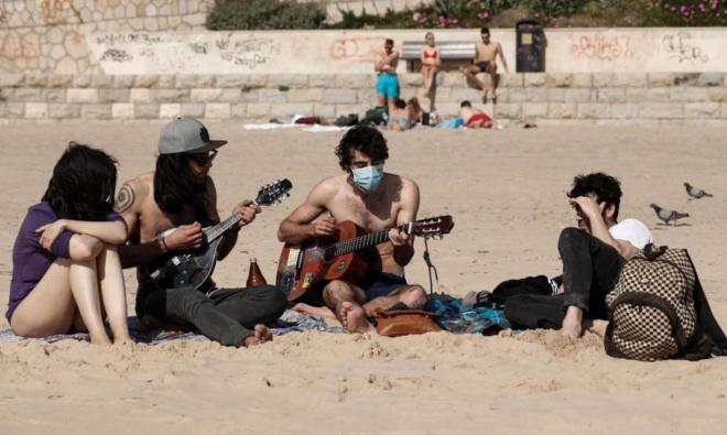 Cuatro jóvenes tocan la guitarra en la playa de Carcavelos, en Portugal.