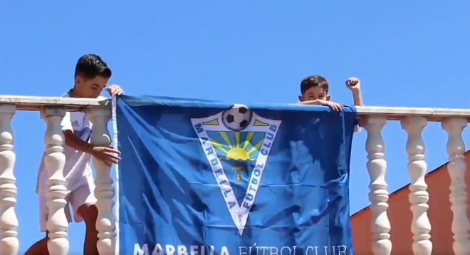 Dos niños sujetan una bandera del Marbella.