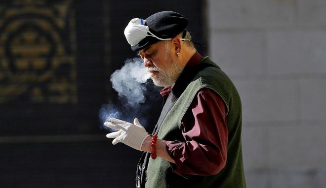 Un hombre se quita la mascarilla para fumar en la calle (Foto: EFE).