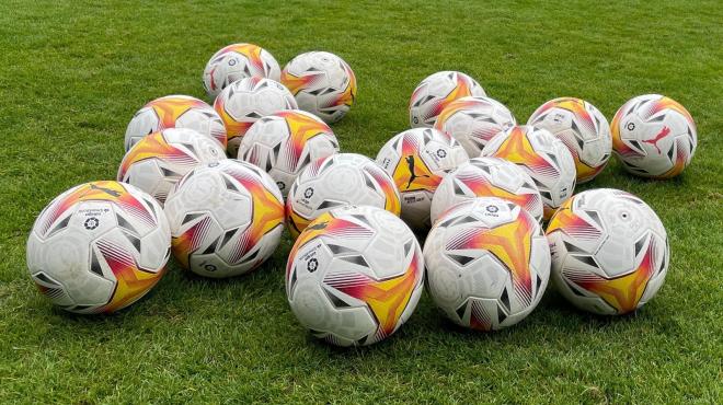 Balones de fútbol esperando en el césped para comenzar un entrenamiento.
