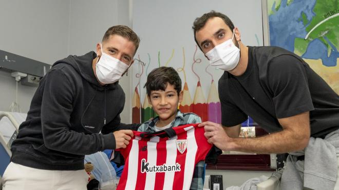 Los Leones del Athletic Club Iker Muniain e Iñigo Lekue entregan una camiseta a un niño hospitalizado.