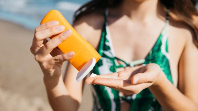 Mujer en la playa echándose crema solar (Freepik)