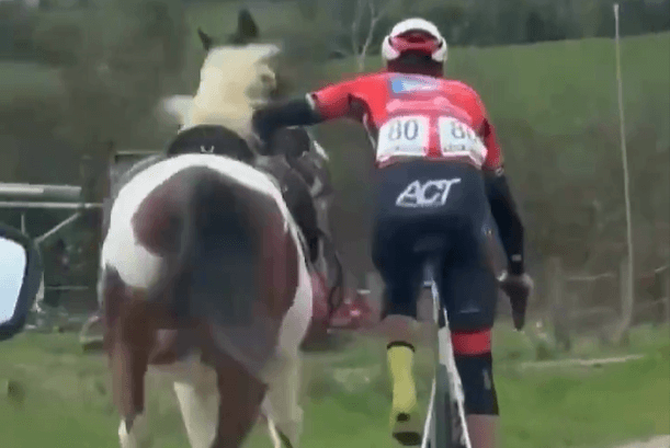 Ciclista doma a un caballo en plena etapa.