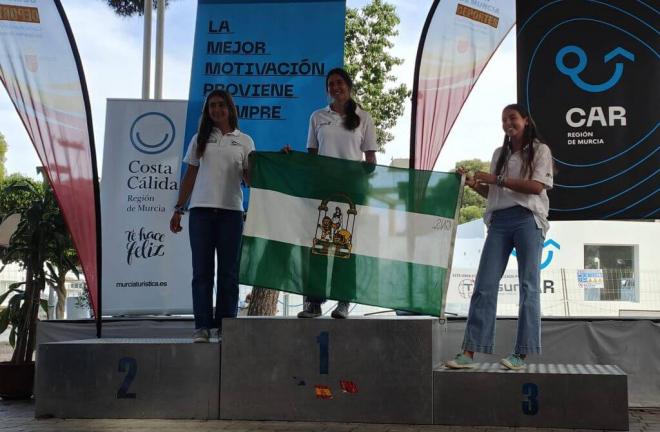 Las andaluzas Olivia Sánchez y Laura Béjar muestran la bandera andaluza en el podio.