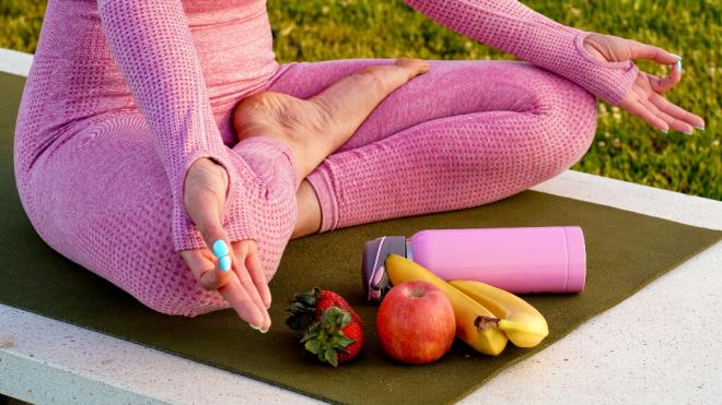 Mujer meditando al aire libre junto con una cantimplora de agua y frutas frescas (Freepik)