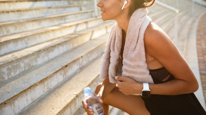 Mujer haciendo deporte con una botella de agua y una toalla sobre los hombros (Foto: Freepik)