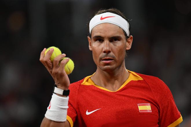 Rafa Nadal sostiene dos pelotas en la mano antes de sacar en el partido de doble con Alcaraz (FOTO: