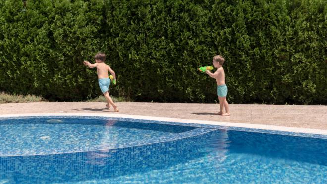 Dos niños jugando con unas pistolas de agua alrededor de una piscina (Fuente: Freepik)