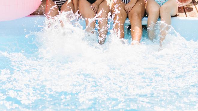 Chicas sentadas en el bordillo de una piscina pataleando el agua (Fuente: Freepik)