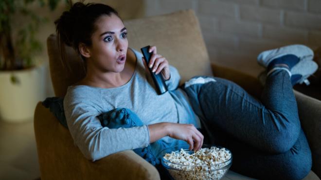 Mujer joven viendo series de televisión sin parar mientras come palomitas (Fuente: Freepik)