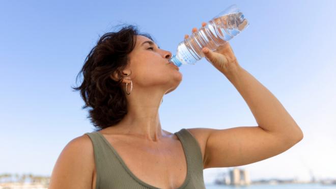 Mujer bebiendo agua de una botella de plástico (Fuente: Freepik)