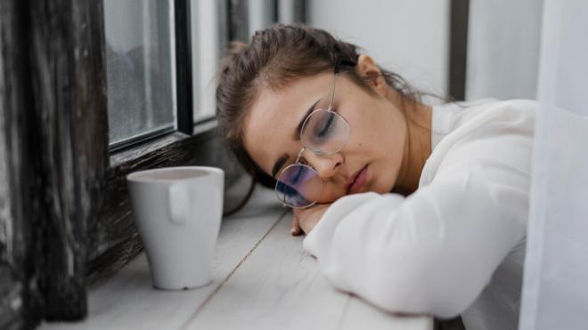 Chica dormida en el alféizar de una ventana con un café al lado (Foto: Freepik)