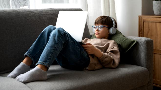 Niño con gafas tumbado en el sofá mientras está con el ordenador (Foto: Freepik)