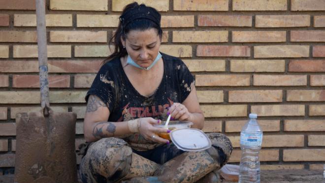 Una voluntaria come en una acera llena de lodo tras el paso de la DANA (Foto: EFE)