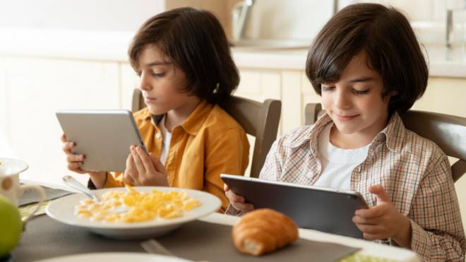 Hermanos gemelos pendientes de las pantallas en el desayuno (Foto: Freepik)