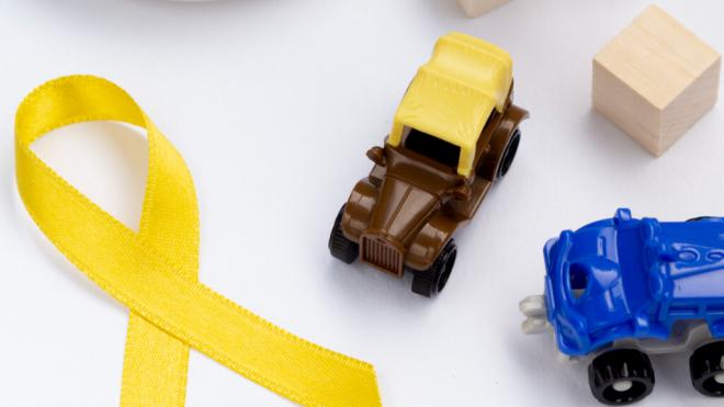 Lazo amarillo del cáncer infantil junto con dos coches de juguete (Foto: Freepik)