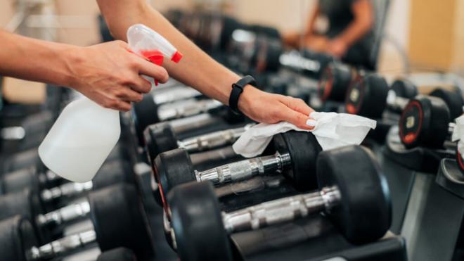 Mujer desinfectando una mancuerna en el gimnasio (Foto: Freepik)