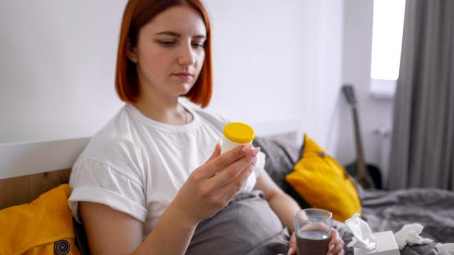 Mujer sentada en el sofá mirando un bote de pastillas (Foto: Freepik)