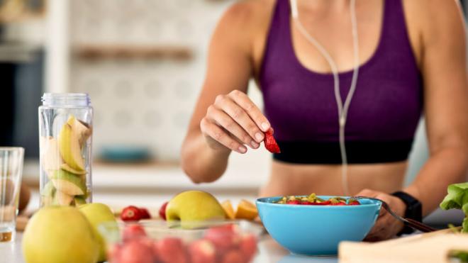 Mujer con ropa deportiva comiendo fruta (Foto: Frepik)