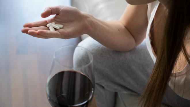 Persona con unas pastillas en una mano y una copa de vino en la otra (Foto: Freepik)