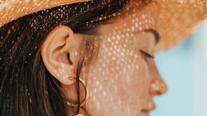 Mujer de perfil protegiéndose del sol con un sombrero (Foto: Freepik)