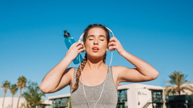 Mujer haciendo deporte al aire libre mientras se coloca los cascos (Foto: Freepik)