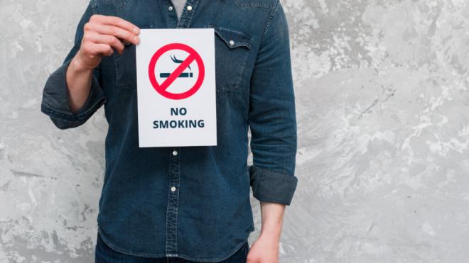 Hombre sujetando un cartel que pone en inglés 'No fumar' (Foto: Freepik)