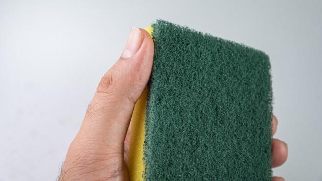 Hombre sujetando un estropajo verde y amarillo (Foto: Freepik)
