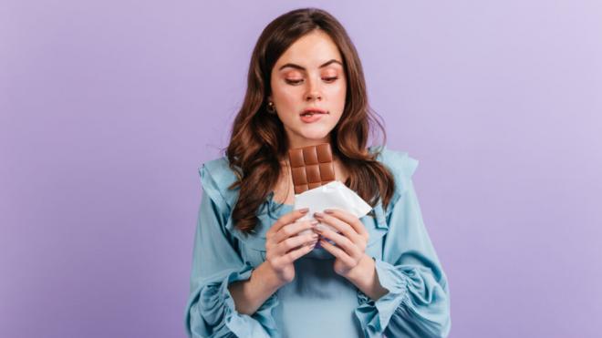 Mujer joven mirando con deseo una tableta de chocolate (Foto: Freepik)