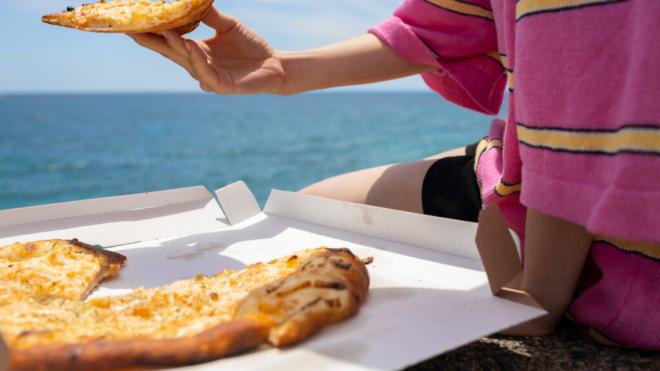 Gente comiendo pizza en la playa (Foto: Freepik)