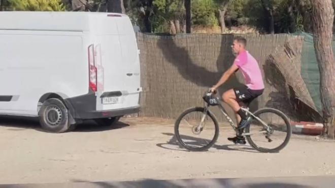 Adrián San Miguel llega en bici al entrenamiento del Real Betis.