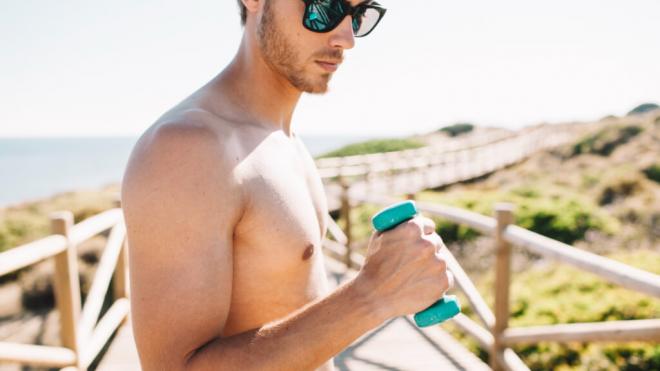 Chico en la playa levantando una mancuerna poco pesada (Foto: Freepik)