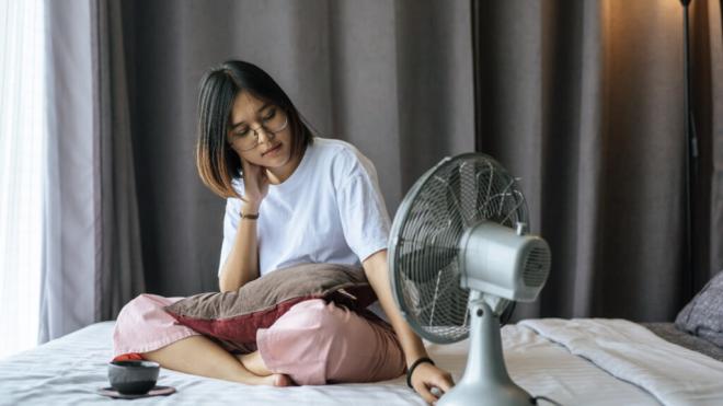 Mujer sobre la cama frente a un ventilador (Foto: Freepik)