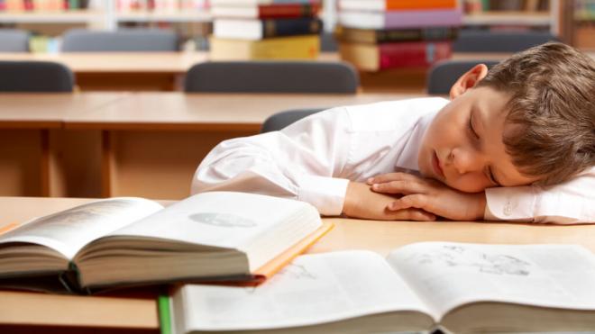 Niño durmiendo en una biblioteca frente a dos libros (Foto: Freepik)