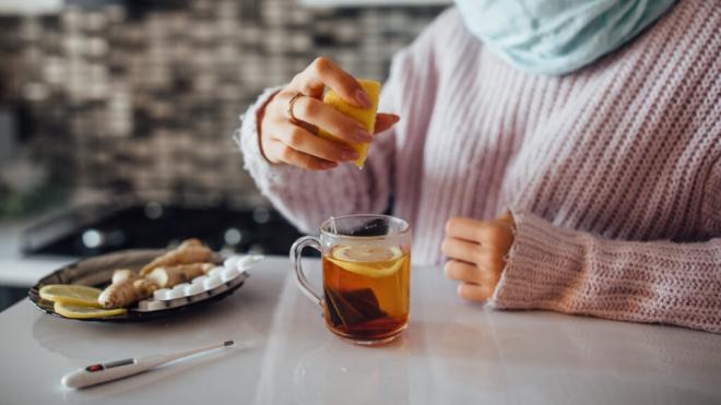 Mujer exprimiendo un limón en una infusión con un blíster de pastillas y un termómetro sobre la mesa (Foto. Freepik)