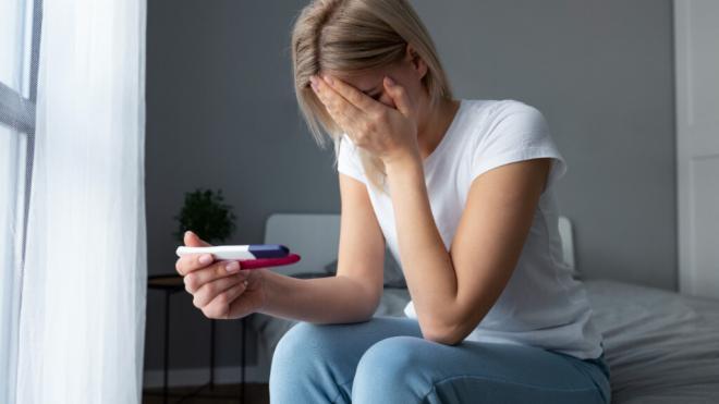 Mujer preocupada al ver el resultado de un test de embarazo (Freepik)