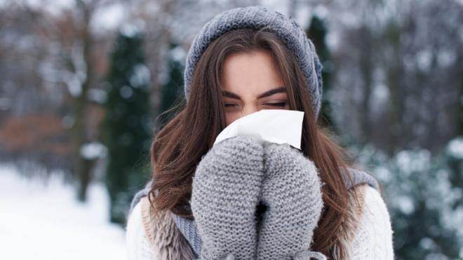 Mujer abrigada en la calle sonándose la nariz (Freepik)